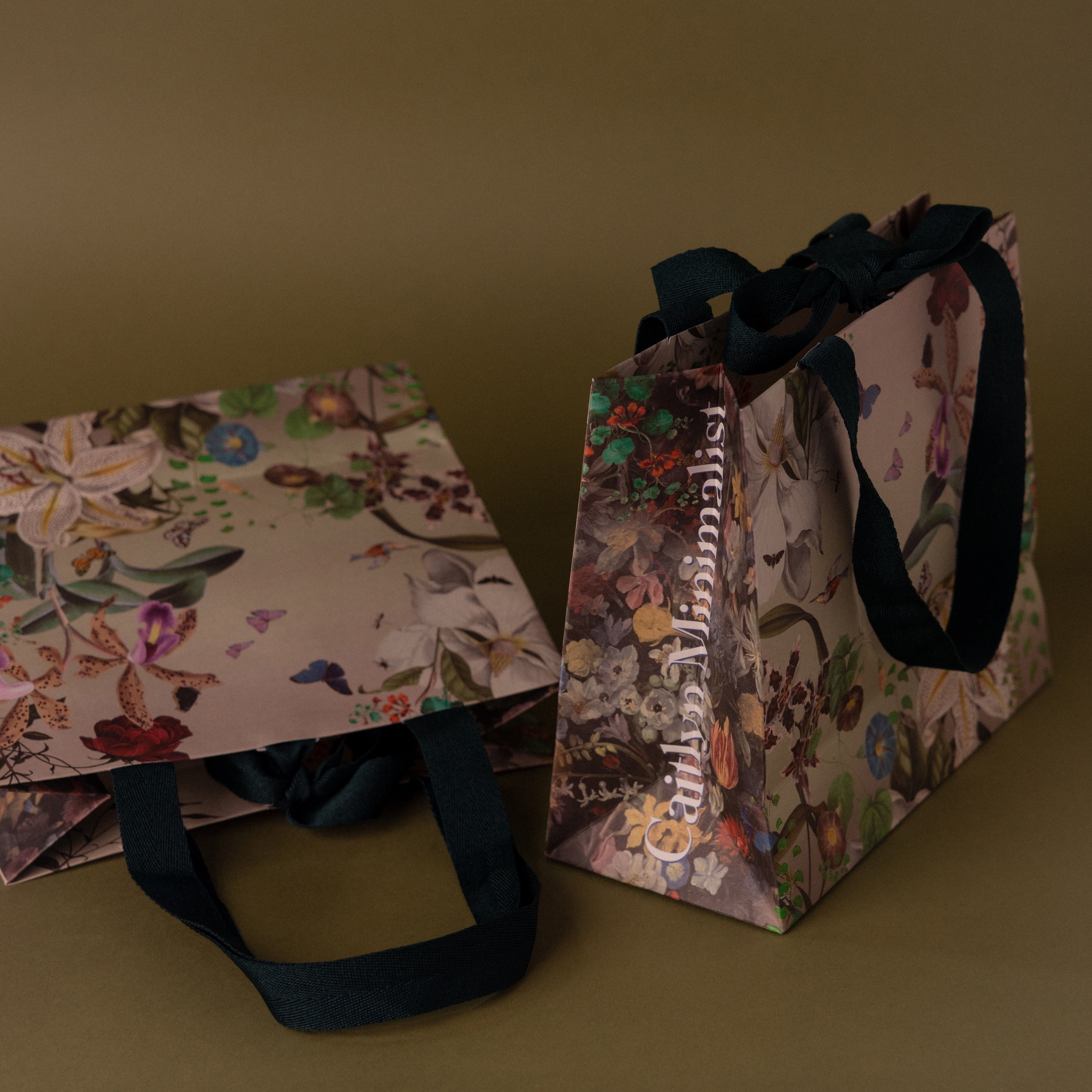 The Floral Gift Bag Add-On features two elegant floral-patterned gift bags with black ribbon handles, providing a special finishing touch—all set against a brown background.