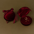 Two Red Velvet Round Ring Boxes, one open to reveal three gold rings, rest elegantly on a brown surface.