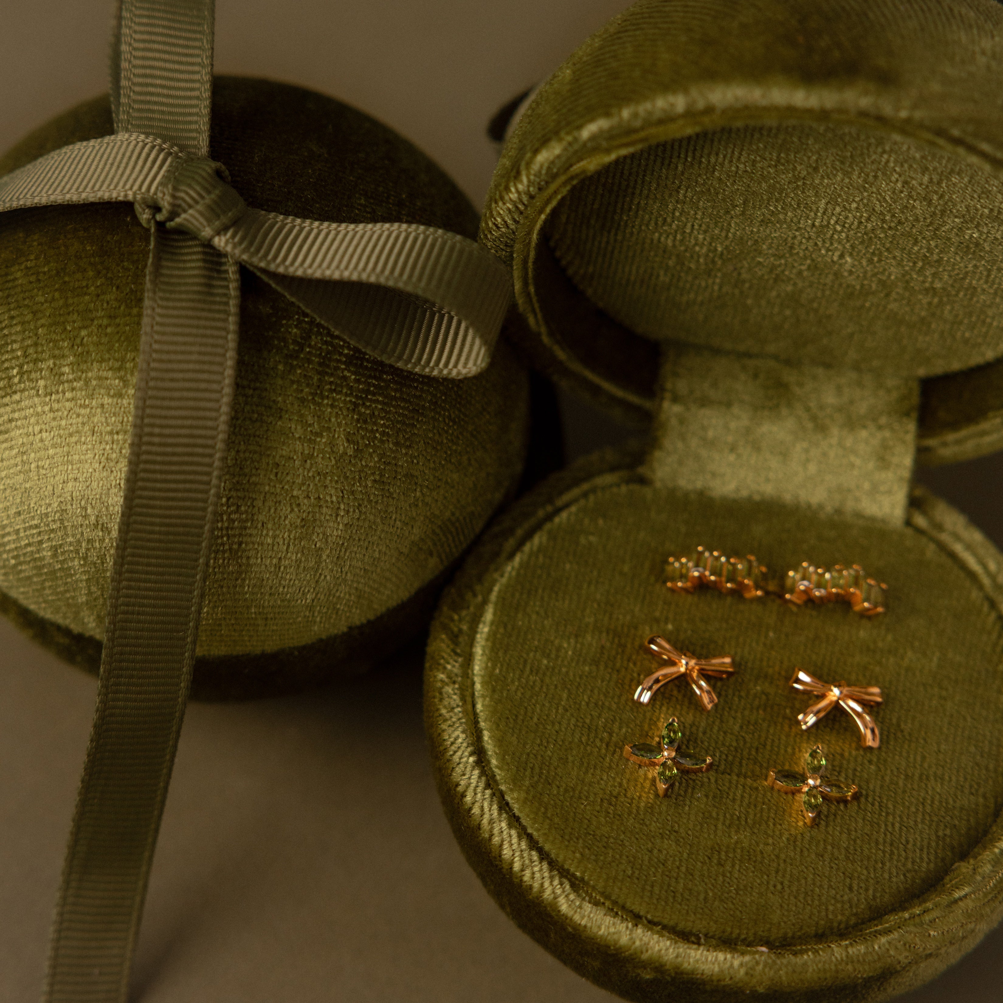 The Green Velvet Round Ring Box elegantly displays three pairs of gold bow and crown-shaped earrings, serving as a chic jewelry or ring holder for your treasured pieces.