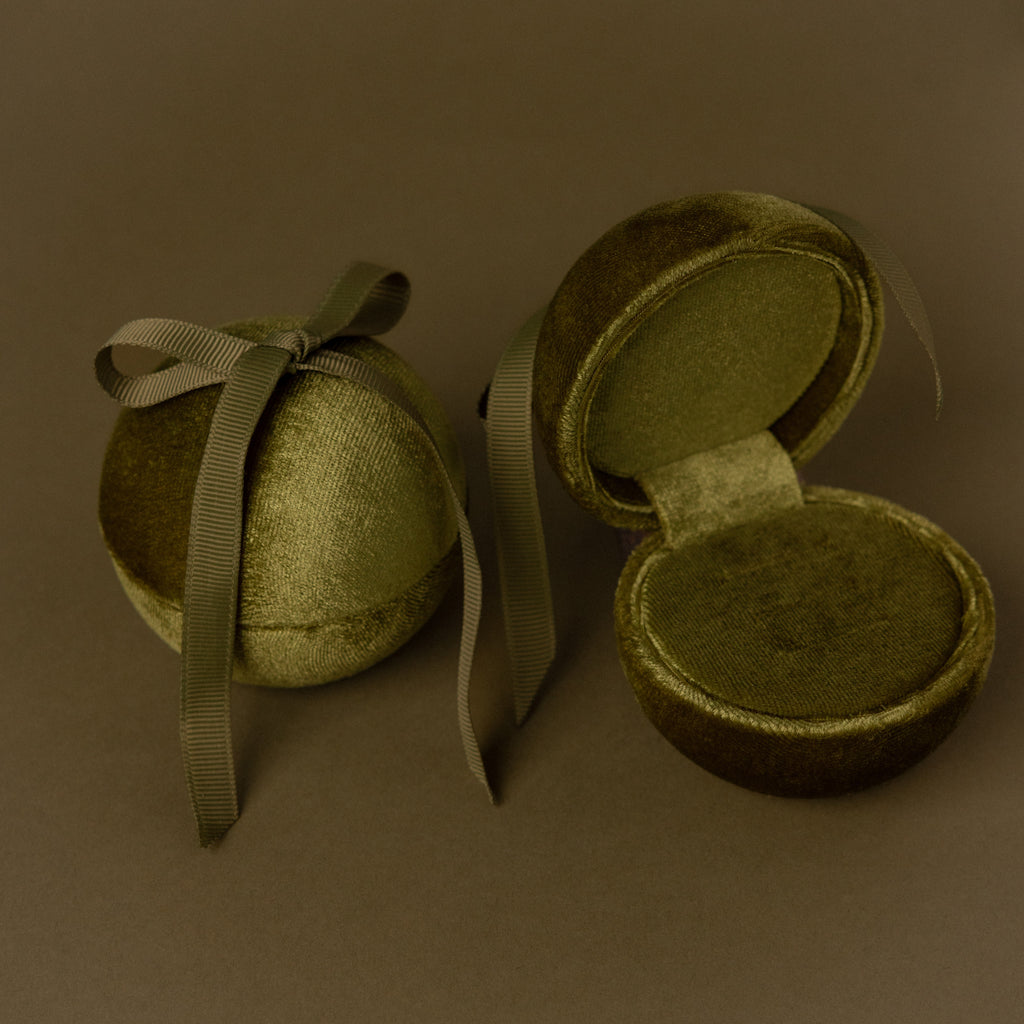Two Green Velvet Round Ring Boxes—one tied with a ribbon and one open to show a ring—serve as elegant jewelry holders against a brown background.