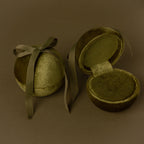 Two Green Velvet Round Ring Boxes—one tied with a ribbon and one open to show a ring—serve as elegant jewelry holders against a brown background.