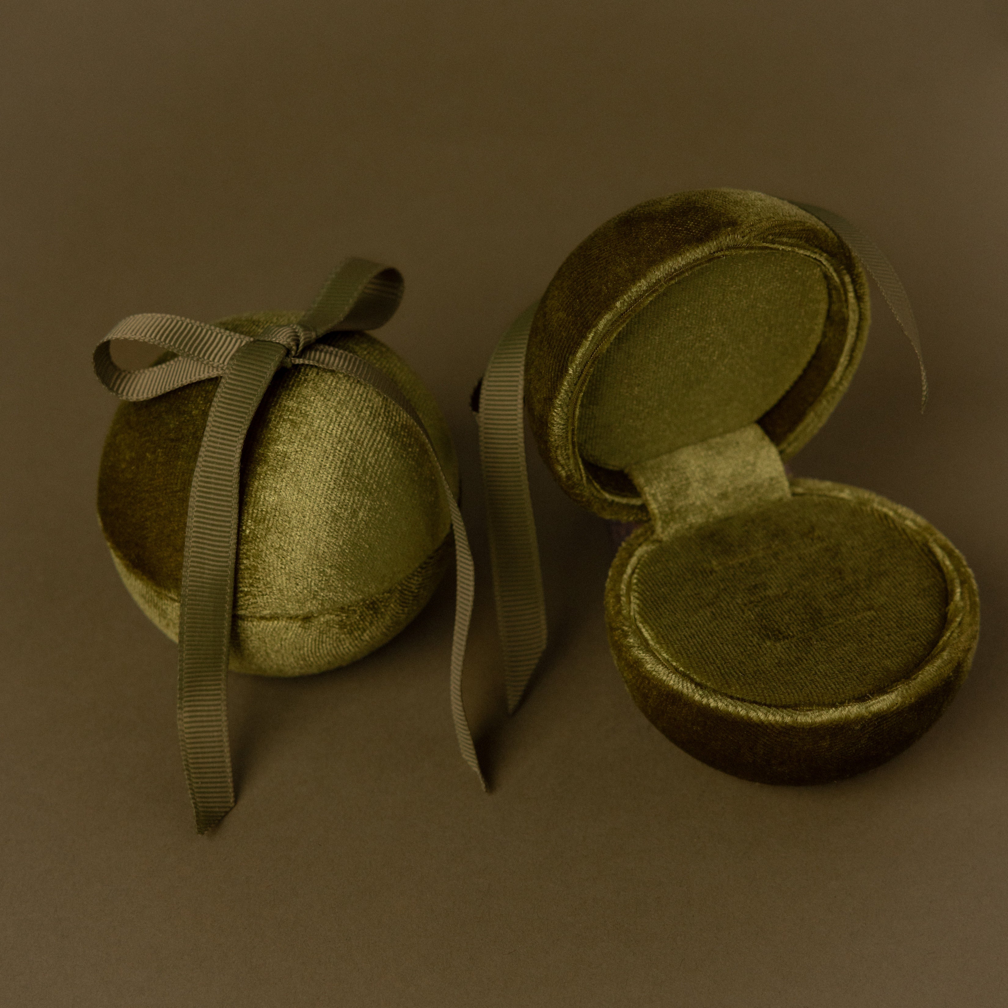 Two Green Velvet Round Ring Boxes—one tied with a ribbon and one open to show a ring—serve as elegant jewelry holders against a brown background.