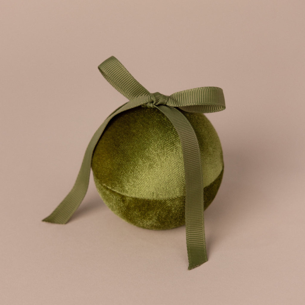 The Green Velvet Round Ring Box, topped with a matching ribbon bow and set against a beige background, creates an elegant look reminiscent of a festive ornament or jewelry keepsake for special occasions.