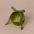 The Green Velvet Round Ring Box, topped with a matching ribbon bow and set against a beige background, creates an elegant look reminiscent of a festive ornament or jewelry keepsake for special occasions.