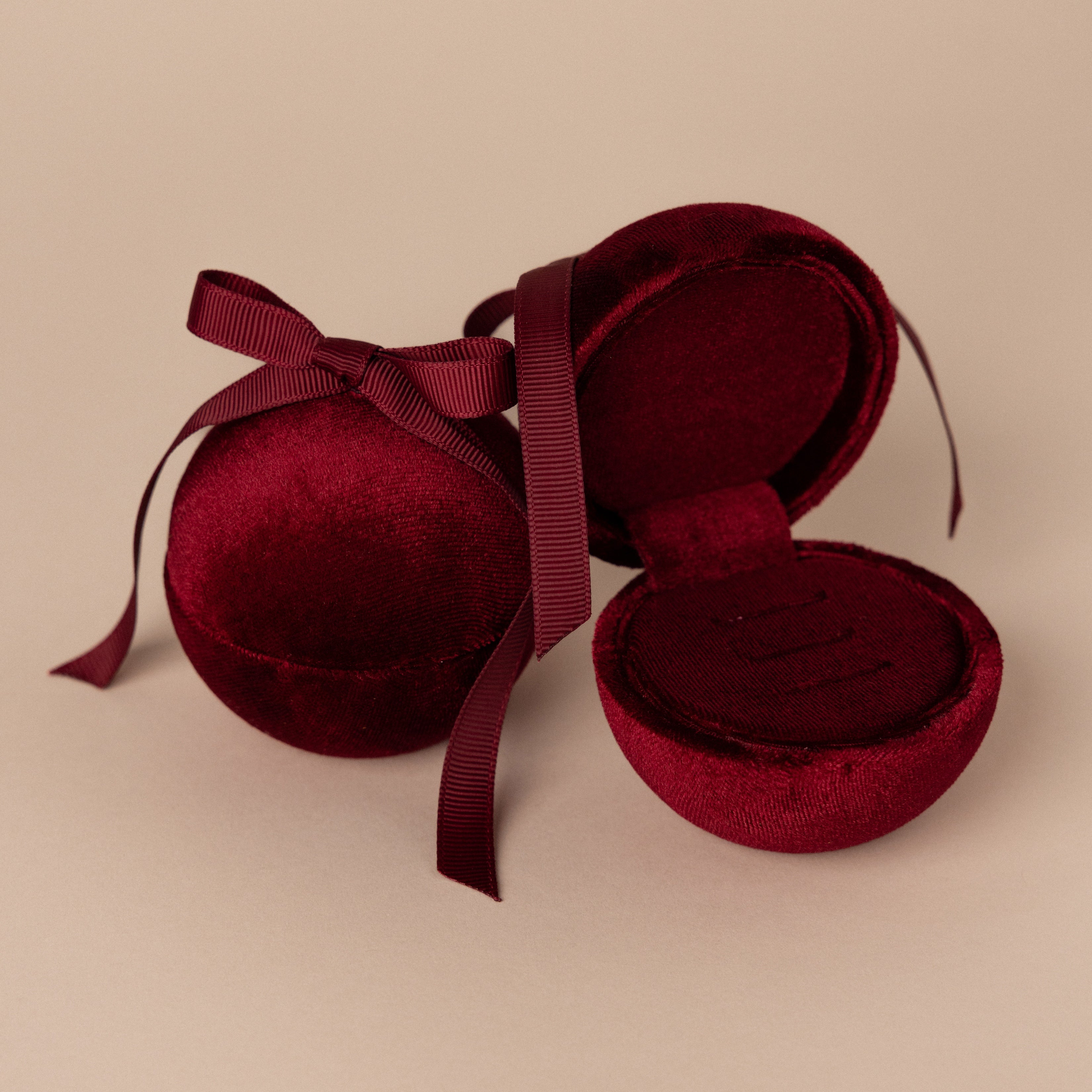 Two Red Velvet Round Ring Boxes—one open as an elegant ring holder, the other closed—are displayed on a beige background.