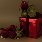 Velvet Round Ring Boxes in red and green, each holding a ring, are arranged around a large red gift box with a ribbon.
