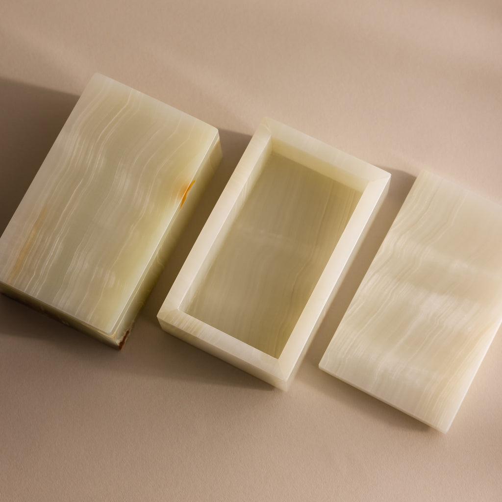 The Green Onyx Jewelry Box, rectangular and handcrafted with a lid, is shown open on a soft beige surface, displaying its smooth, creamy green texture.