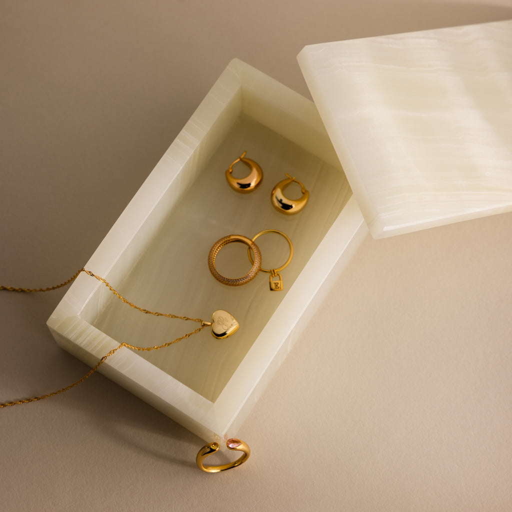 Gold jewelry pieces, including rings, earrings, and a necklace, rest in an open handcrafted Green Onyx Jewelry Box displayed on a beige surface.