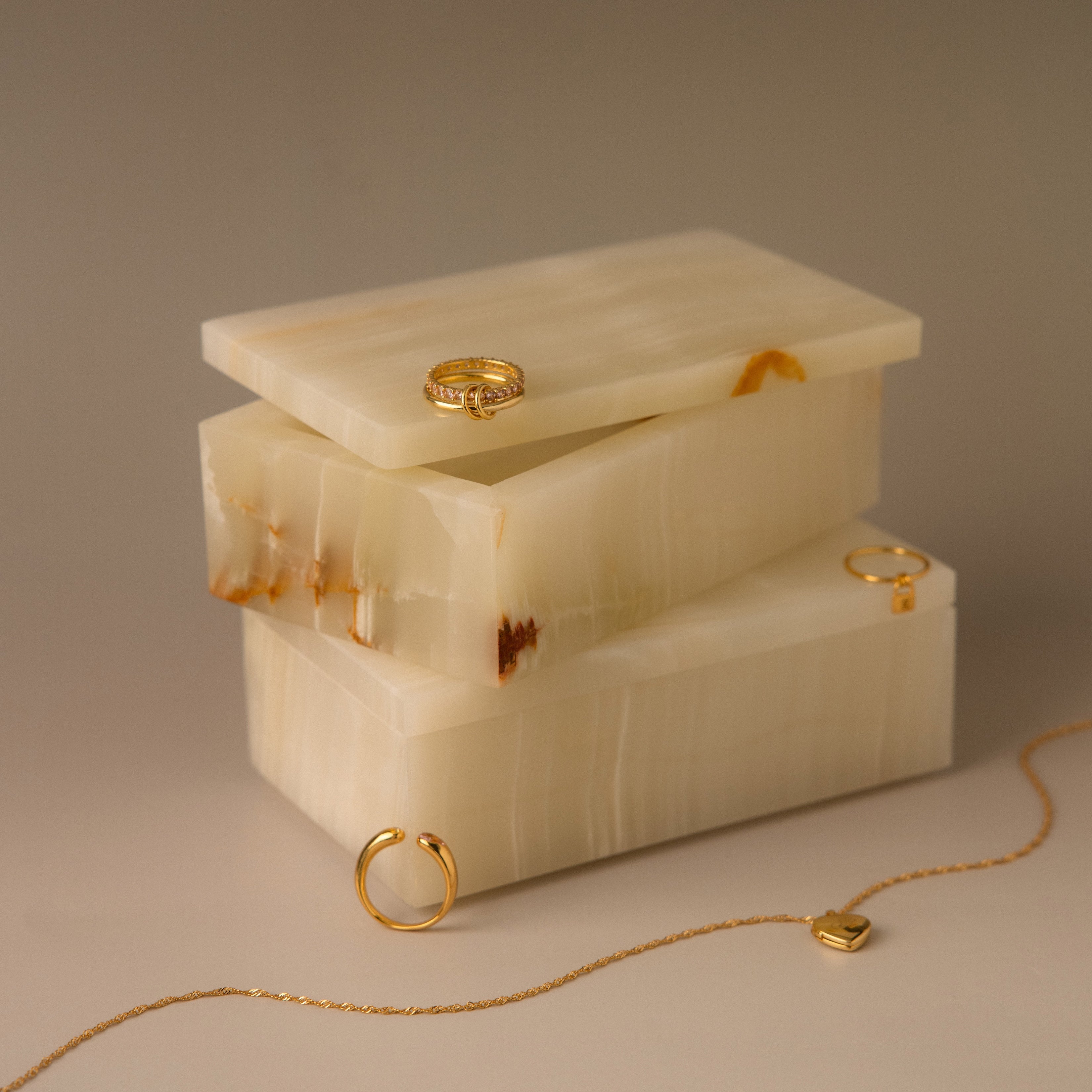 The Green Onyx Jewelry Box is stacked with gold rings and a necklace elegantly displayed on and around it.