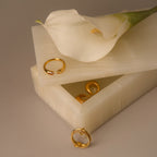 Gold rings and a white calla lily rest on a handcrafted Green Onyx Jewelry Box with a cream-colored stone finish, its lid slightly open.