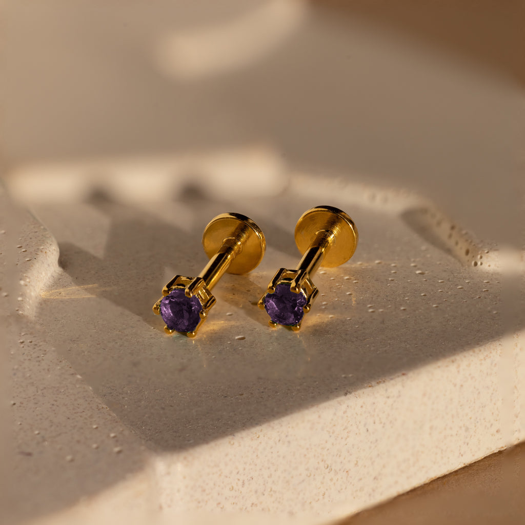 Amethyst Flatback Studs with purple gemstones are shown on a textured, light-colored surface under soft lighting.