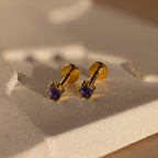 Amethyst Flatback Studs with purple gemstones are shown on a textured, light-colored surface under soft lighting.