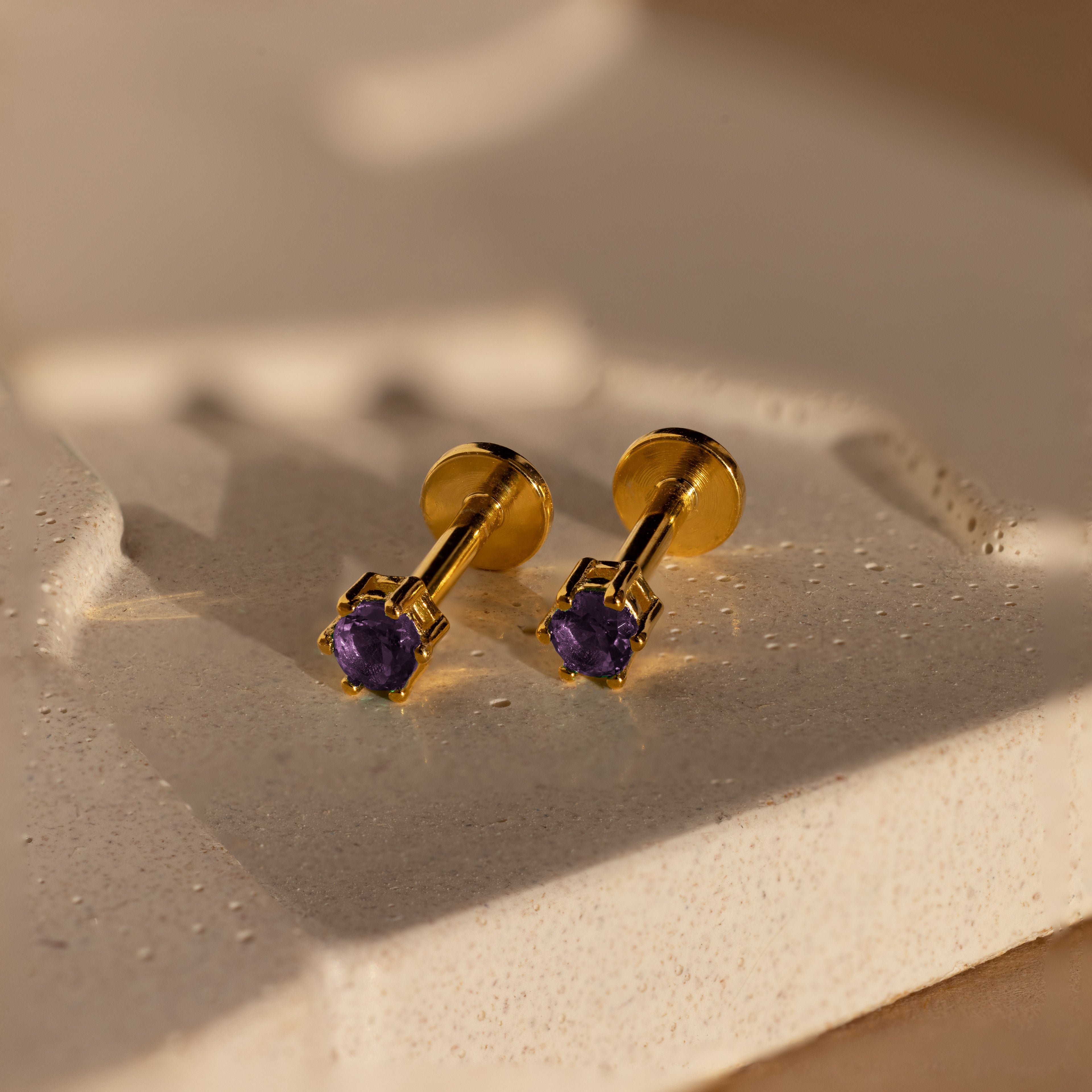 Amethyst Flatback Studs with purple gemstones are shown on a textured, light-colored surface under soft lighting.