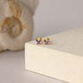 Butterfly Amethyst Flatback Studs with purple stones rest on a soft beige surface with a shell backdrop—ideal for those wanting personalized jewelry.
