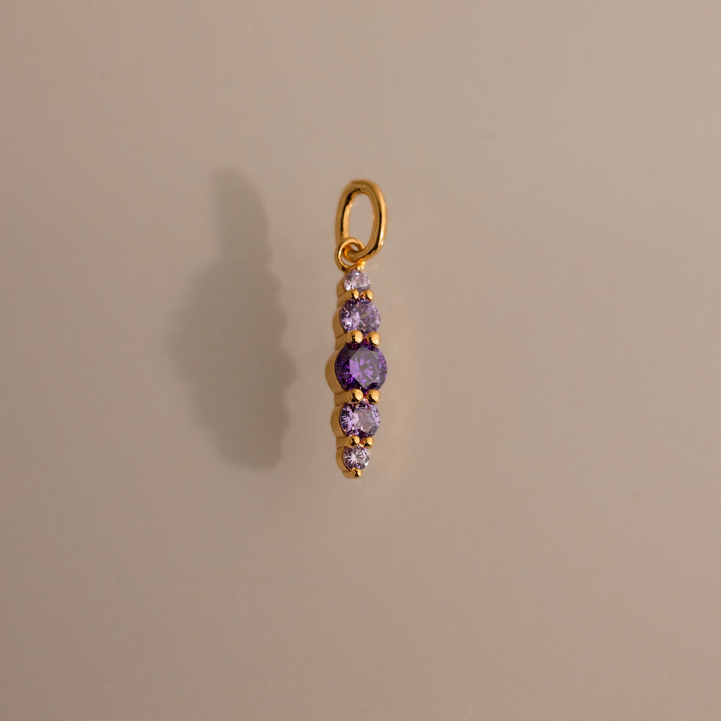 The Ombre Lace Amethyst Charm features five vertically arranged purple gemstones and casts a shadow on a beige background—an ideal personalized birth month gift.