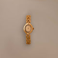The Petite Oval Link Timepiece, a vintage-inspired gold-tone watch with a chain-link band, is displayed on a plain beige background.