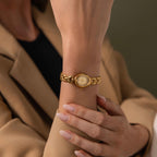 A person wearing the Petite Oval Link Timepiece, a vintage-inspired gold-tone watch, paired with a beige blazer and neatly manicured nails.