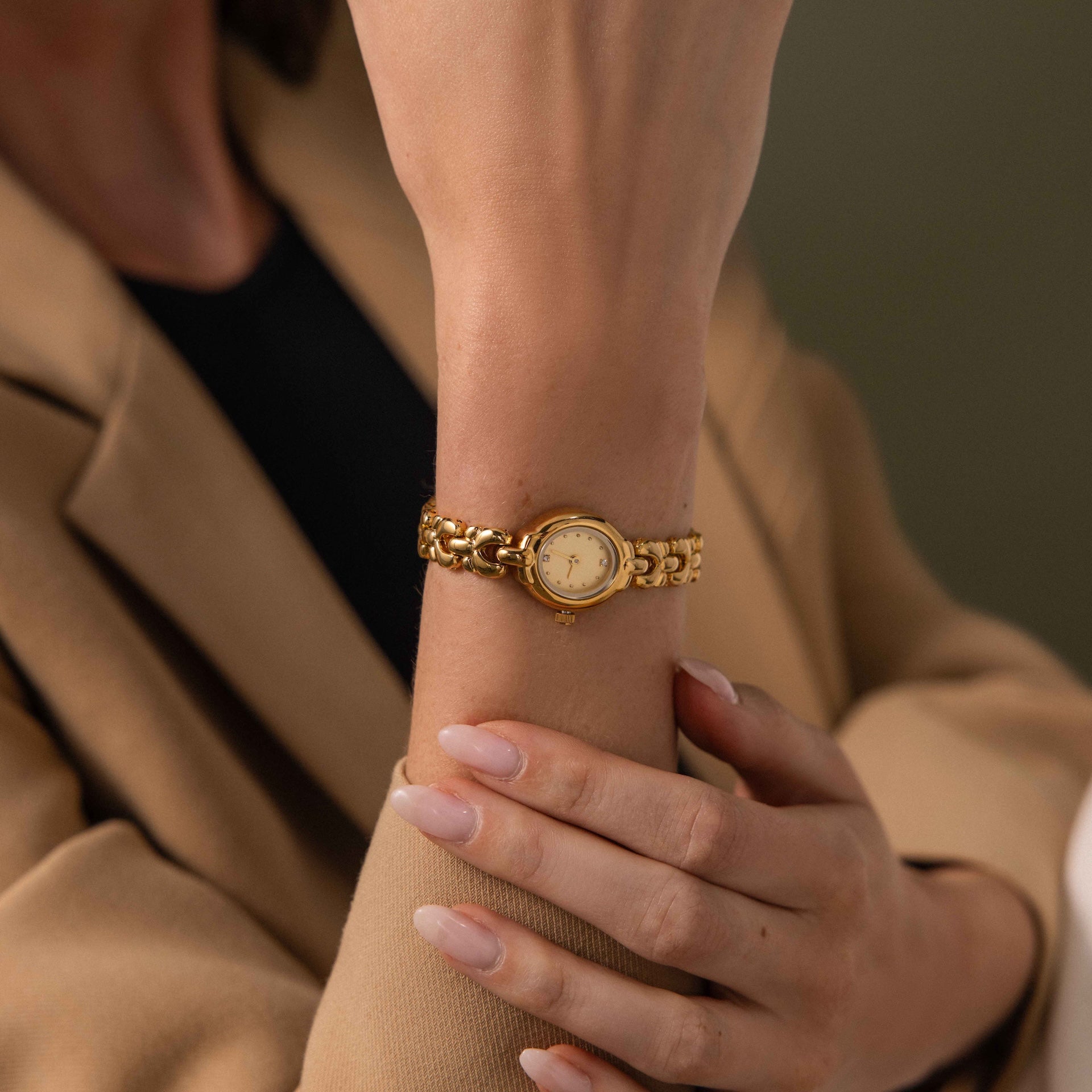 A person wearing the Petite Oval Link Timepiece, a vintage-inspired gold-tone watch, paired with a beige blazer and neatly manicured nails.