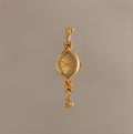 The Floral Twist Timepiece is a gold-tone bracelet watch with a floral-patterned face, marquise-shaped dial, and decorative bow accents on the band.