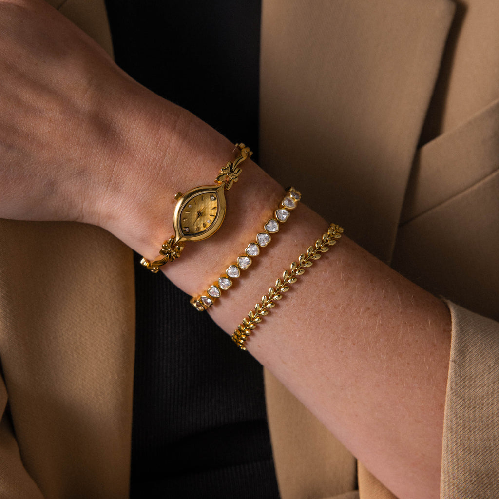 A wrist styled with the Floral Twist Timepiece, showcasing a marquise-shaped dial and gold bracelets, perfectly paired with a beige blazer and black top.