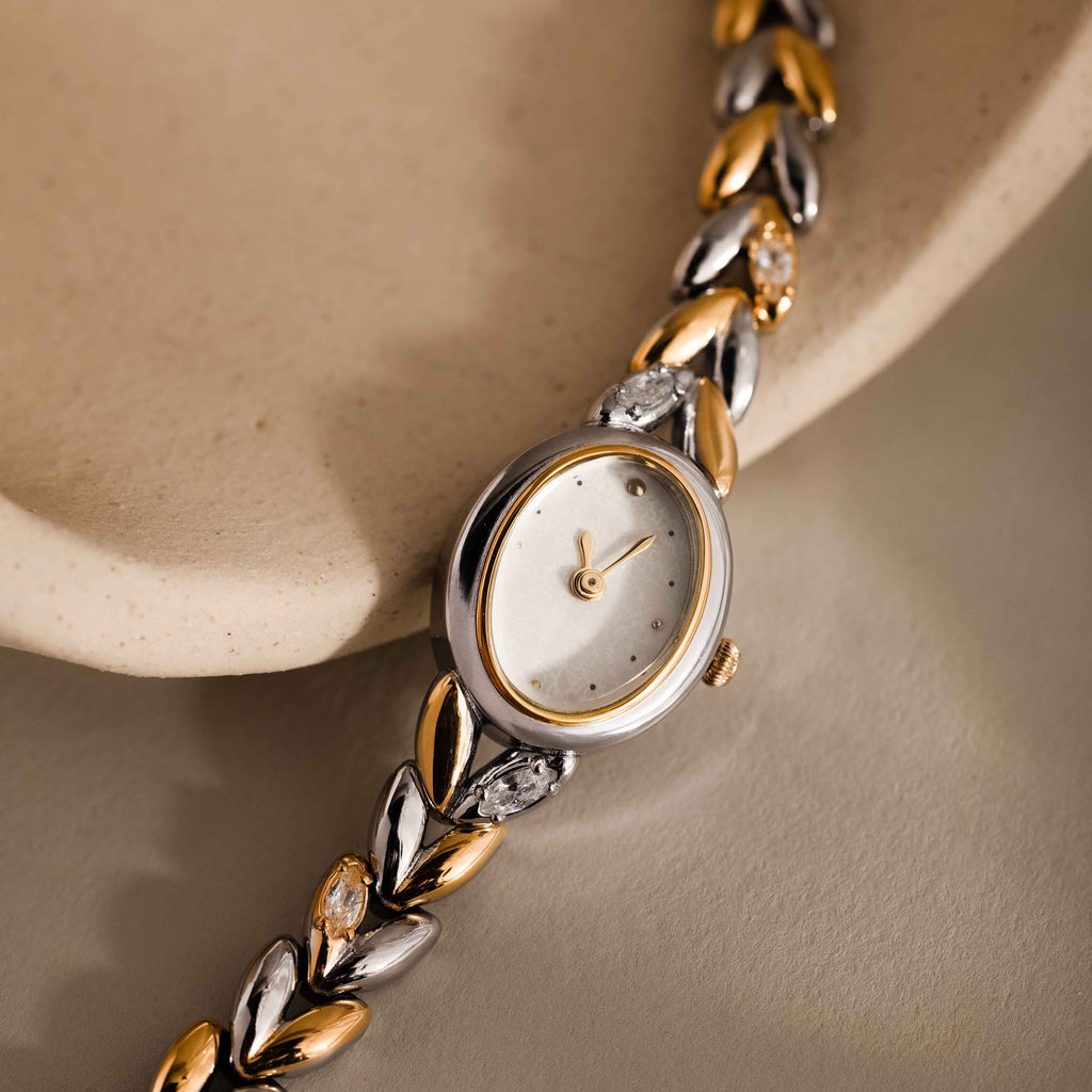 Chevron Diamond Link Timepiece in Mixed Metal, featuring a gold-tone leaf-patterned band, displayed elegantly on a cream-colored ceramic surface.