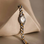 The Chevron Diamond Link Timepiece, featuring a gold-tone face and silver chain-link band, rests elegantly against a beige geometric shape.