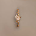 The Chevron Diamond Link Timepiece in Mixed Metal, featuring a round face and chevron-patterned band, is displayed on a plain beige background.