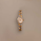 The Chevron Diamond Link Timepiece in Mixed Metal, featuring a round face and chevron-patterned band, is displayed on a plain beige background.