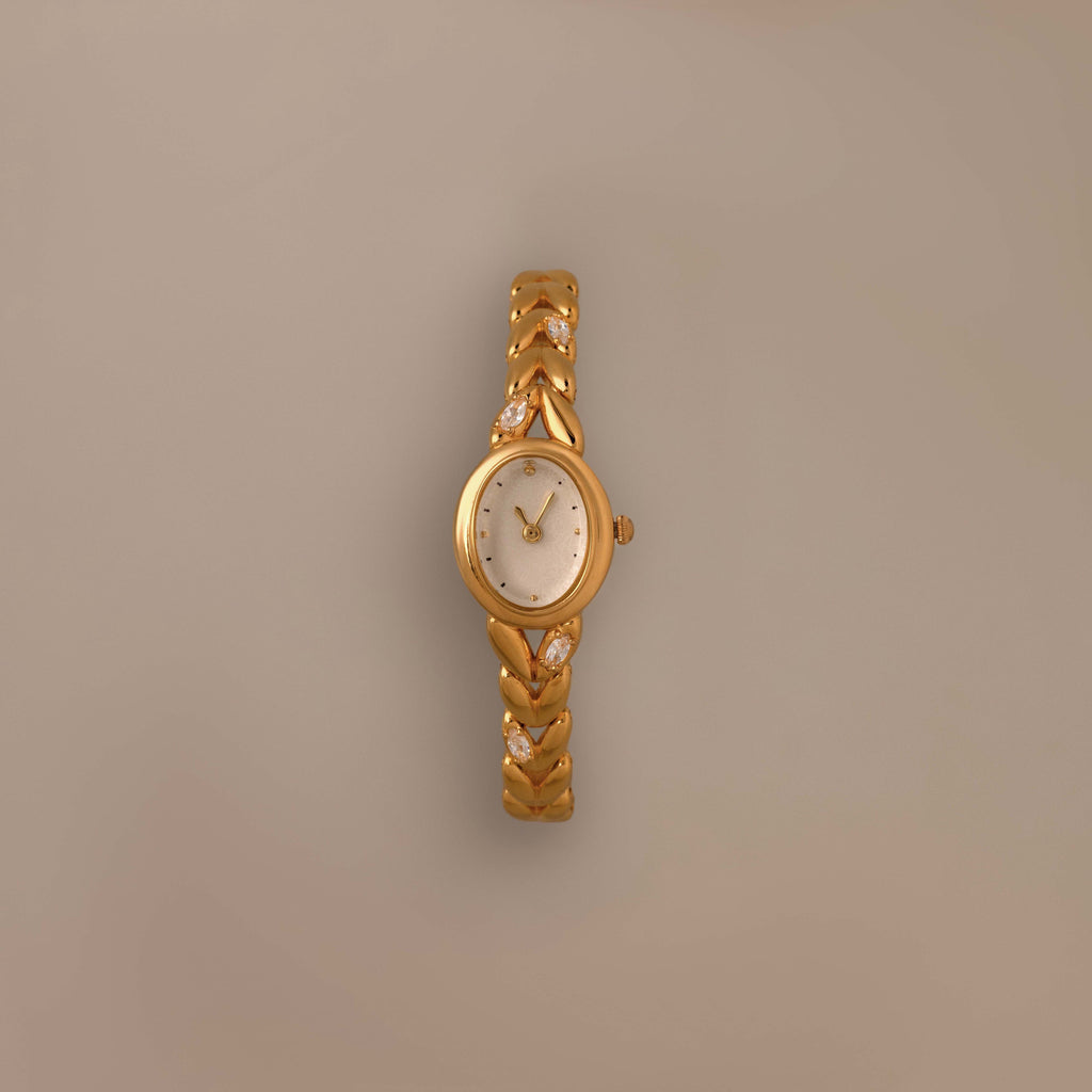Chevron Diamond Link Timepiece featuring a gold-tone braided band and round face, shown against a plain beige background.