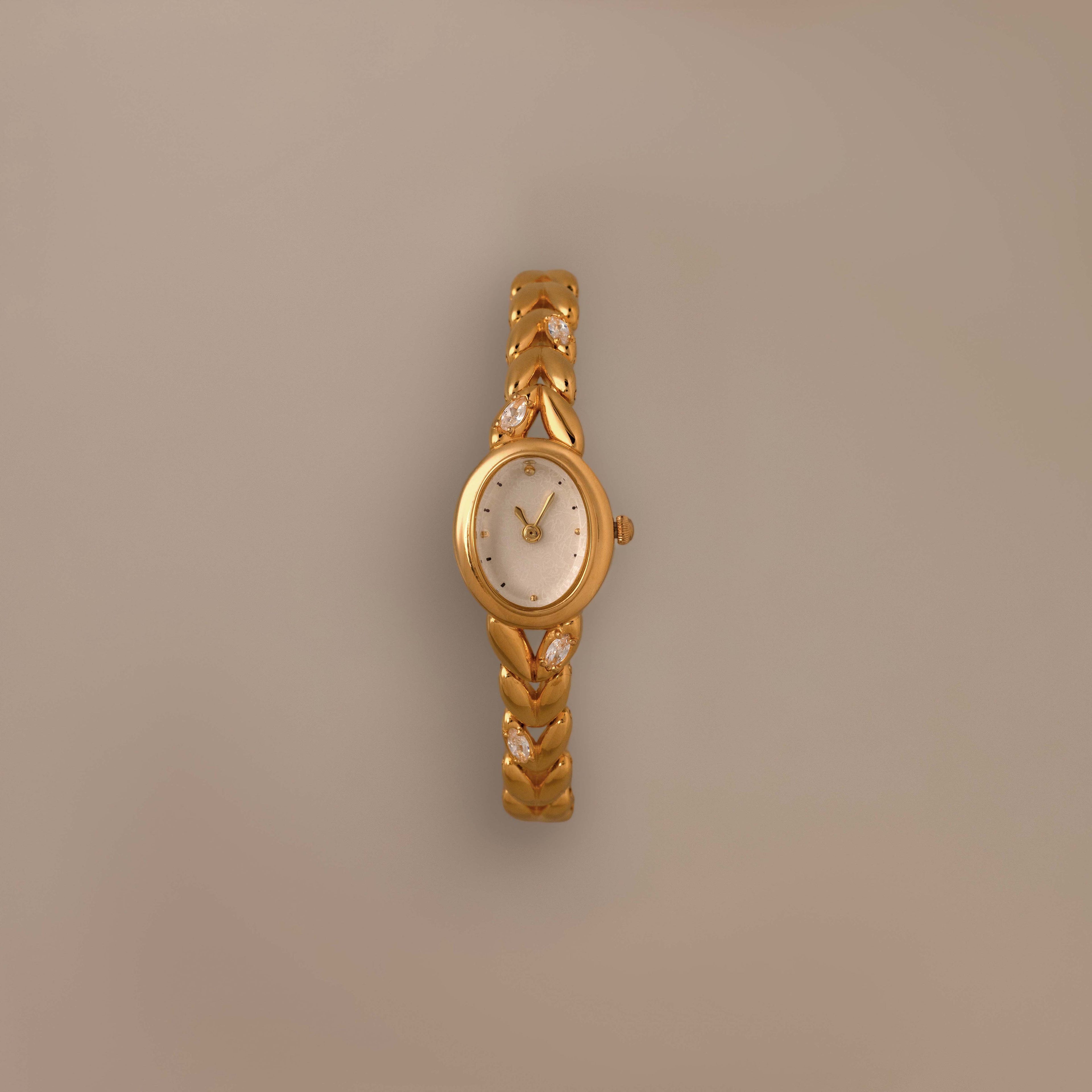 Chevron Diamond Link Timepiece featuring a gold-tone braided band and round face, shown against a plain beige background.
