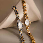 The Chevron Diamond Link Timepiece, an elegant wristwatch with a silver chevron design and leaf-pattern band, is beautifully displayed on a beige surface.