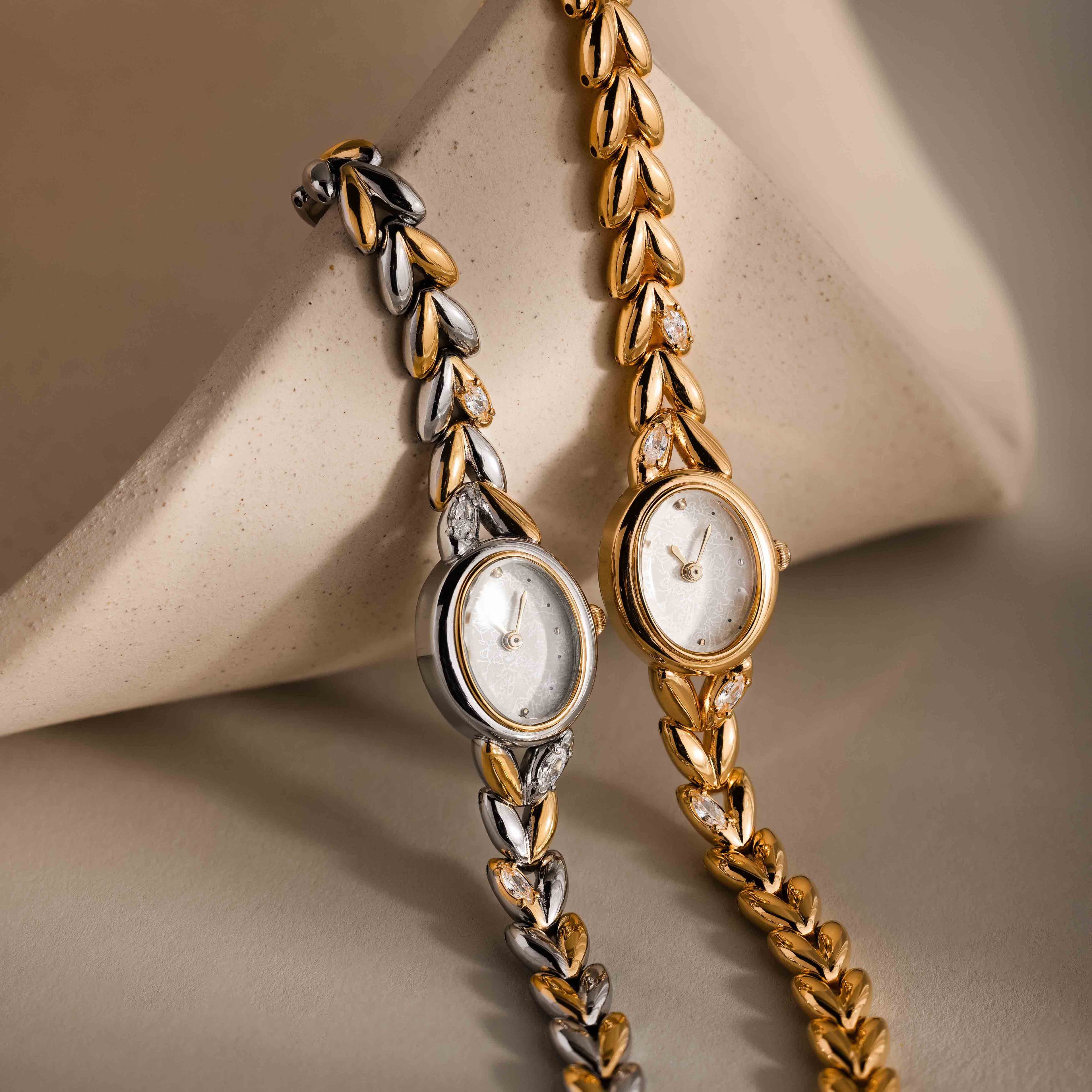 The Chevron Diamond Link Timepiece, an elegant wristwatch with a silver chevron design and leaf-pattern band, is beautifully displayed on a beige surface.