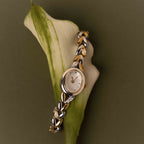 The Chevron Diamond Link Timepiece in Mixed Metal rests atop a white calla lily against an olive green background.