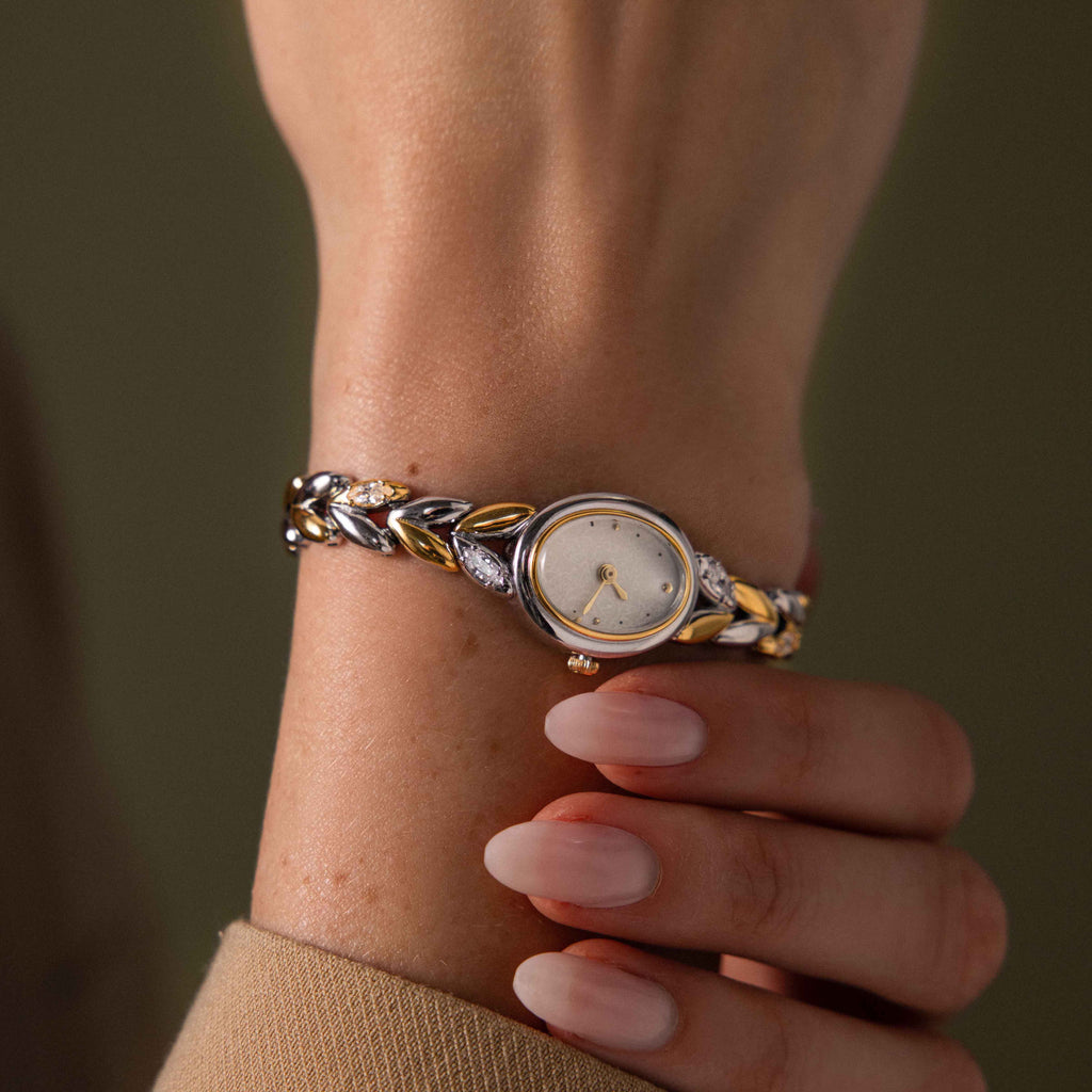 A hand with manicured nails wears the Chevron Diamond Link Timepiece in Mixed Metal, paired elegantly with a sparkling diamond bracelet on the wrist.