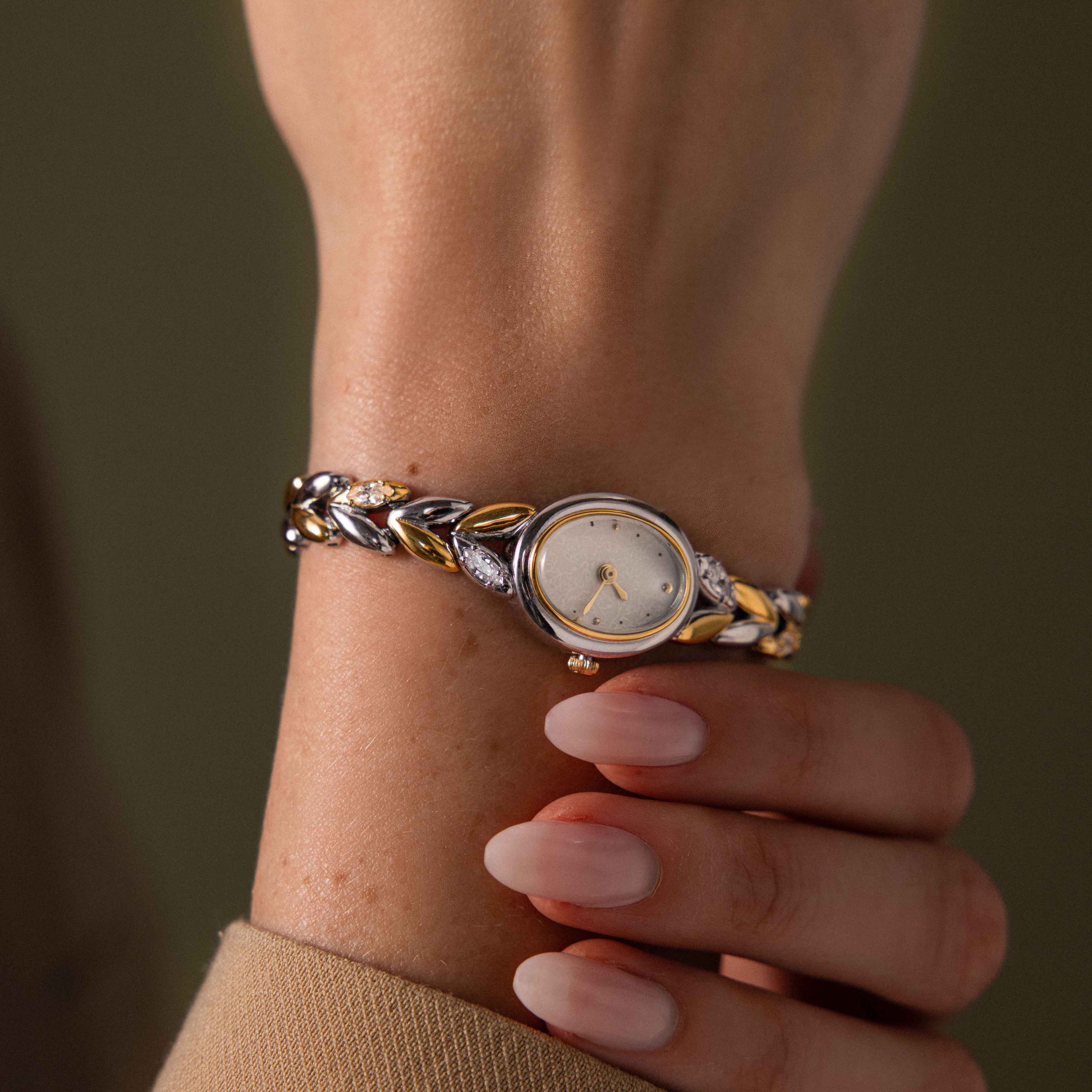 A hand with manicured nails wears the Chevron Diamond Link Timepiece in Mixed Metal, paired elegantly with a sparkling diamond bracelet on the wrist.