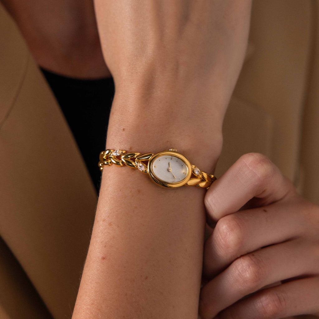 Someone wearing the Chevron Diamond Link Timepiece, a gold-tone watch with a chain-link band, on their left wrist.
