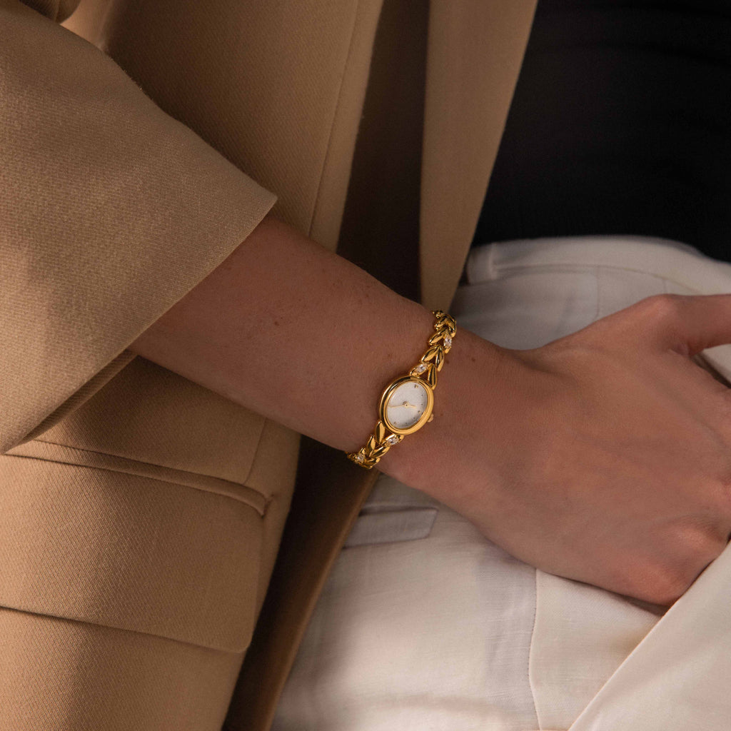A person wearing the Chevron Diamond Link Timepiece in 18K Gold and a beige blazer with a black top and white pants.