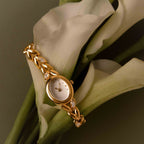 Chevron Diamond Link Timepiece in 18K Gold displayed with a chevron link bracelet over white calla lilies on a muted green background.