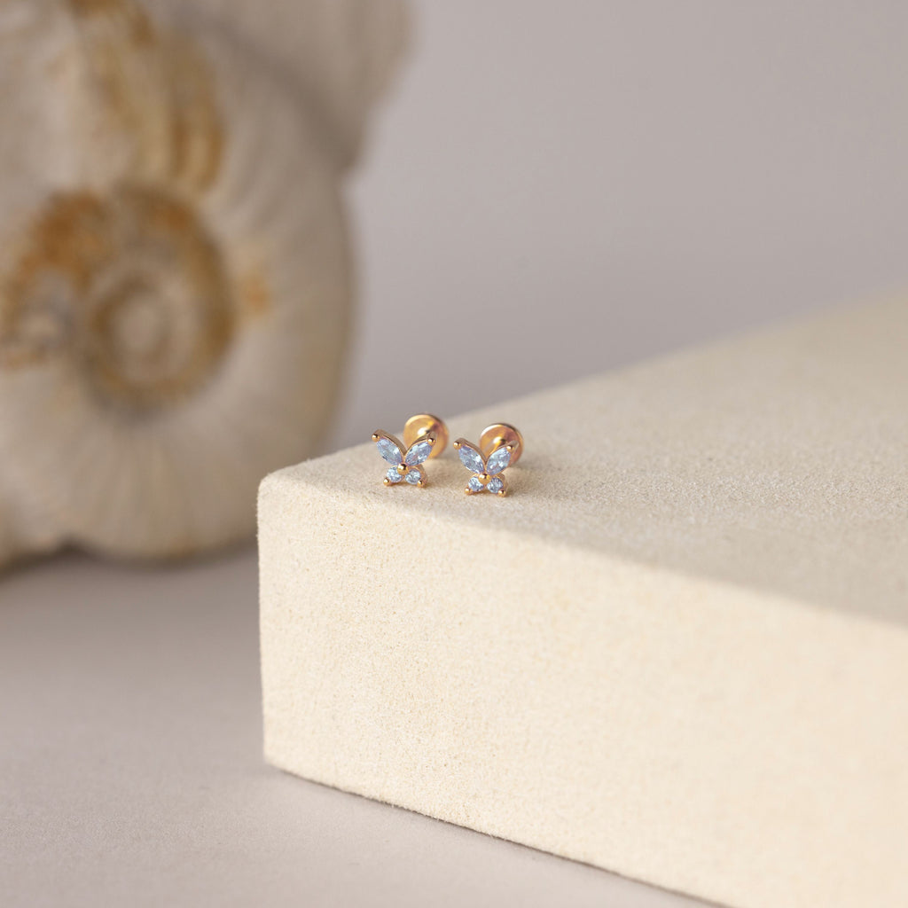 Butterfly Aquamarine Flatback Studs with sparkling stones displayed on a cream-colored surface, seashell in the background—a perfect personalized gift.