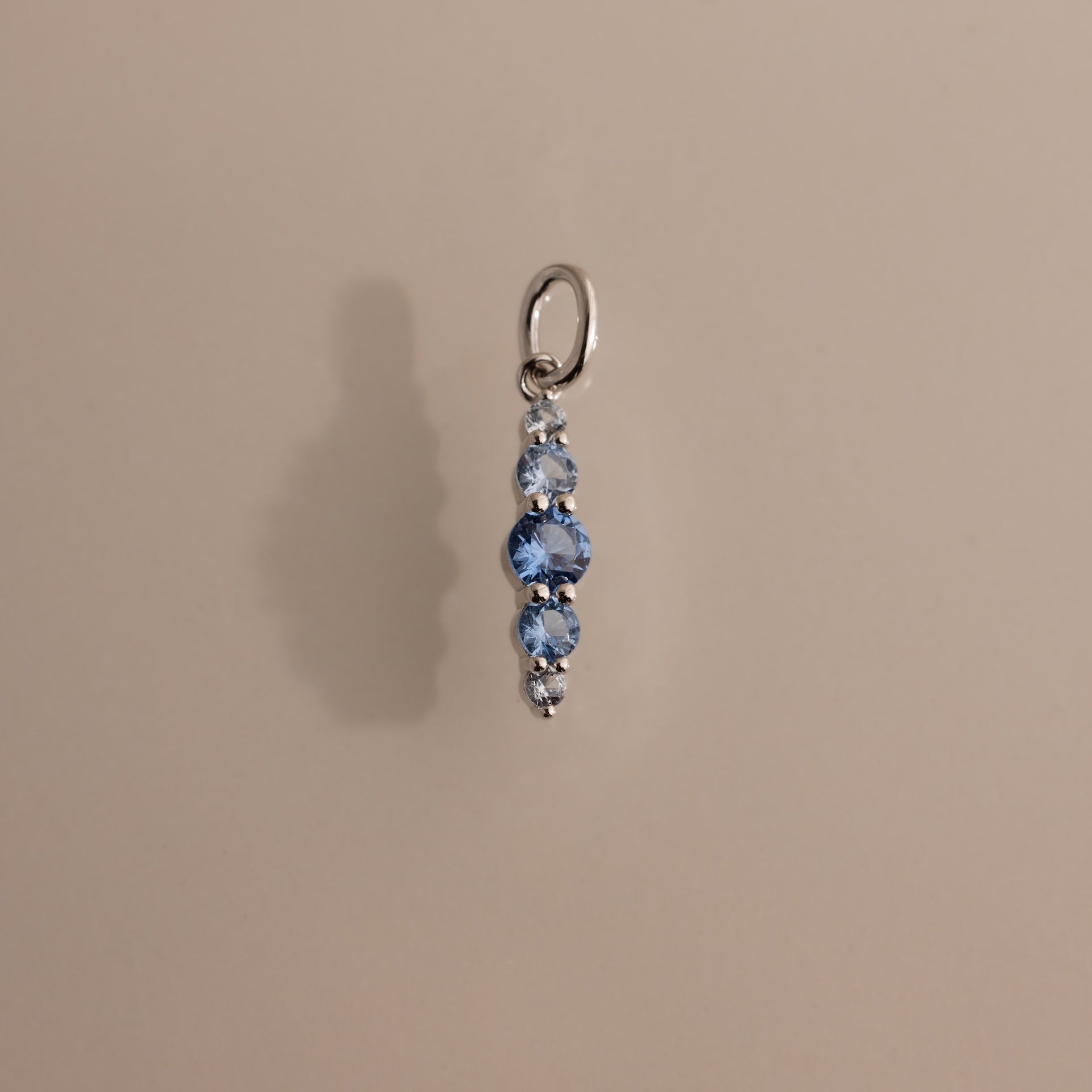 The Ombre Lace Aquamarine Charm features four vertically arranged blue gemstones on a silver pendant—ideal as a personalized accessory or meaningful birth month gift.