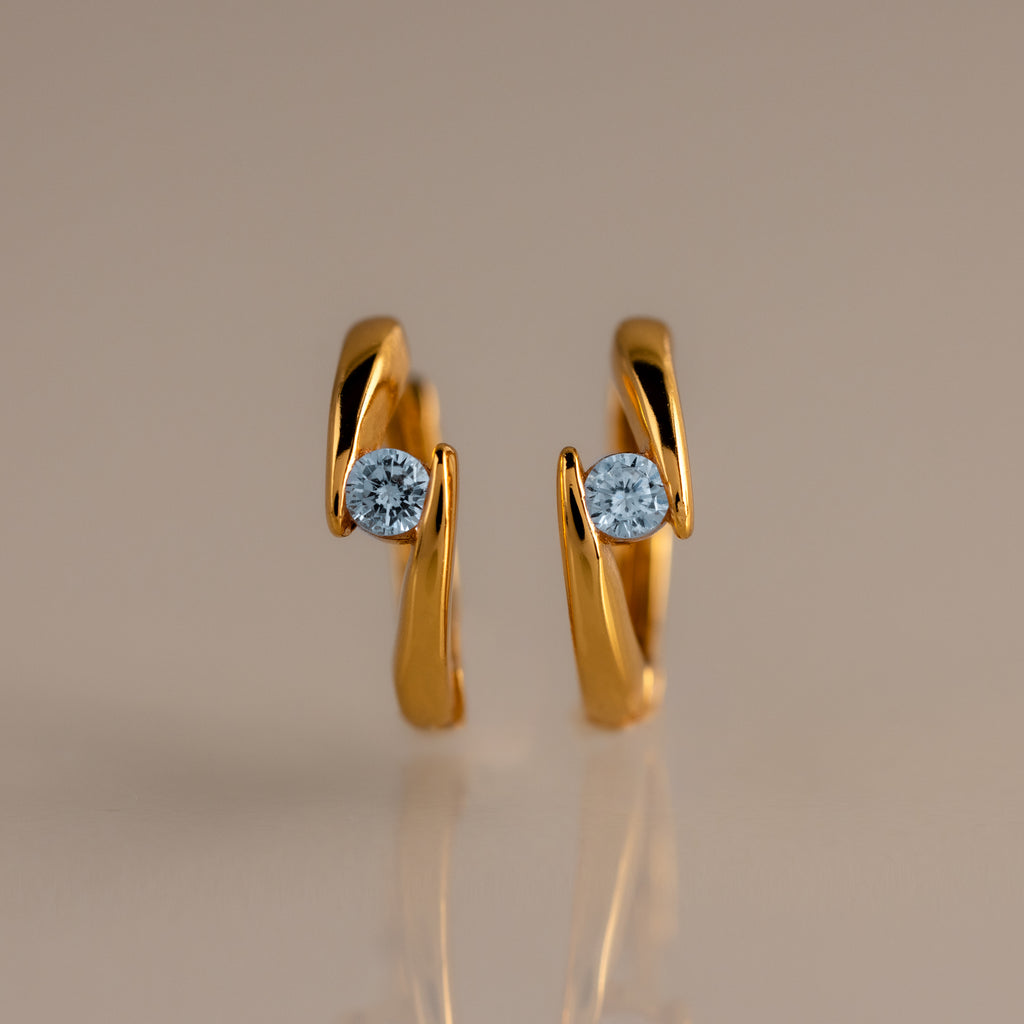 Floating Aquamarine Huggies: gold hoop earrings with a curved design, each set with a single round blue aquamarine—ideal for fans of personalized jewelry.