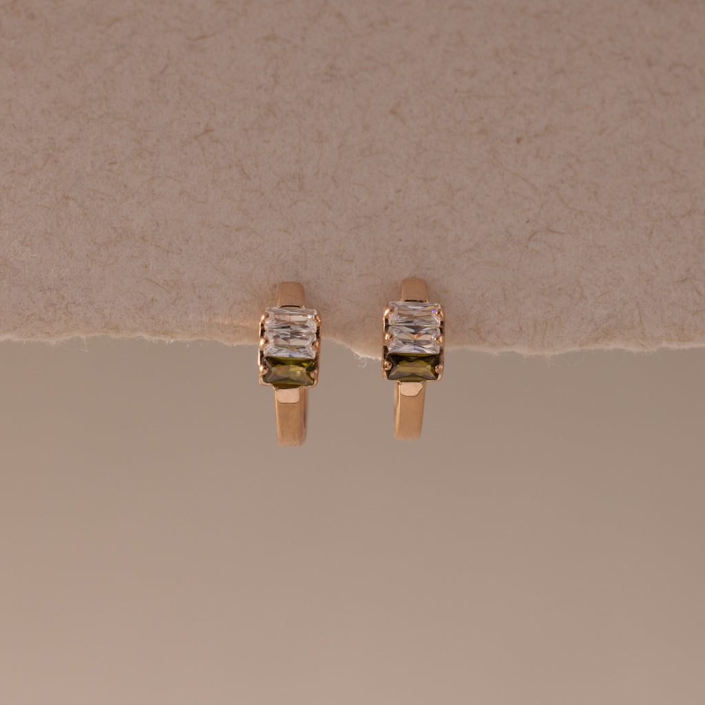 Multiple Baguette Birthstone Huggies in Rose Gold, featuring petite rectangular stones, are displayed on a textured beige background, combining timeless elegance with a modern feel.