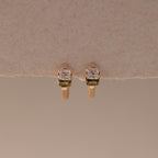 Multiple Baguette Birthstone Huggies in Rose Gold, featuring petite rectangular stones, are displayed on a textured beige background, combining timeless elegance with a modern feel.