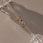 Multiple Baguette Birthstone Huggies, featuring vibrant gemstones, are showcased on the stem of an upside-down glass, casting soft shadows.