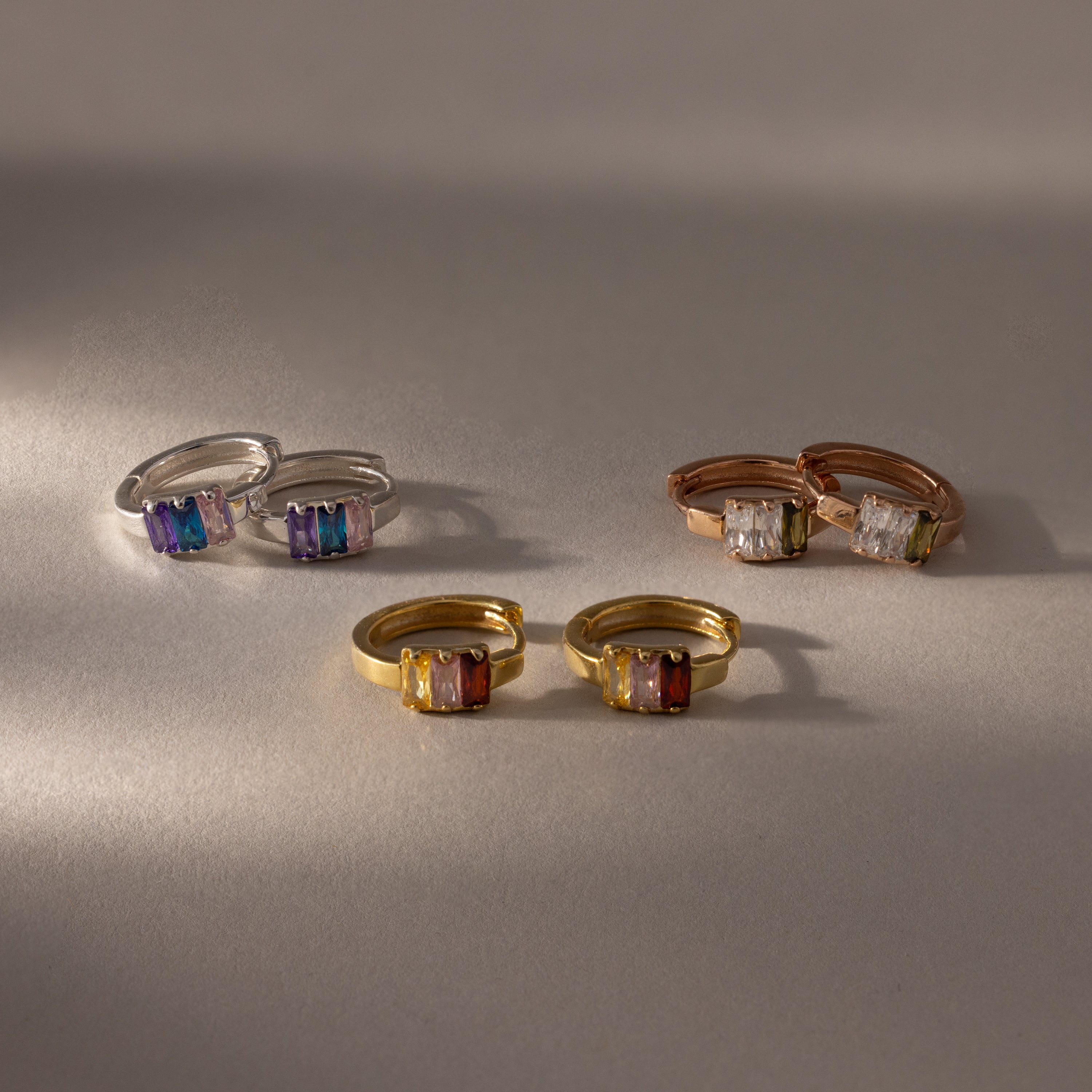 Four pairs of rose gold Multiple Baguette Birthstone Huggies displayed on a neutral surface—perfect for adding colorful jewelry to your collection.
