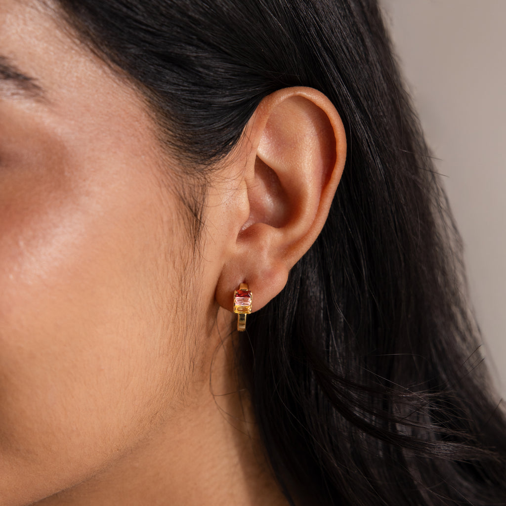 Close-up of a woman's ear wearing Multiple Baguette Birthstone Huggies with a small red gemstone, adding a pop of color to her jewelry look.