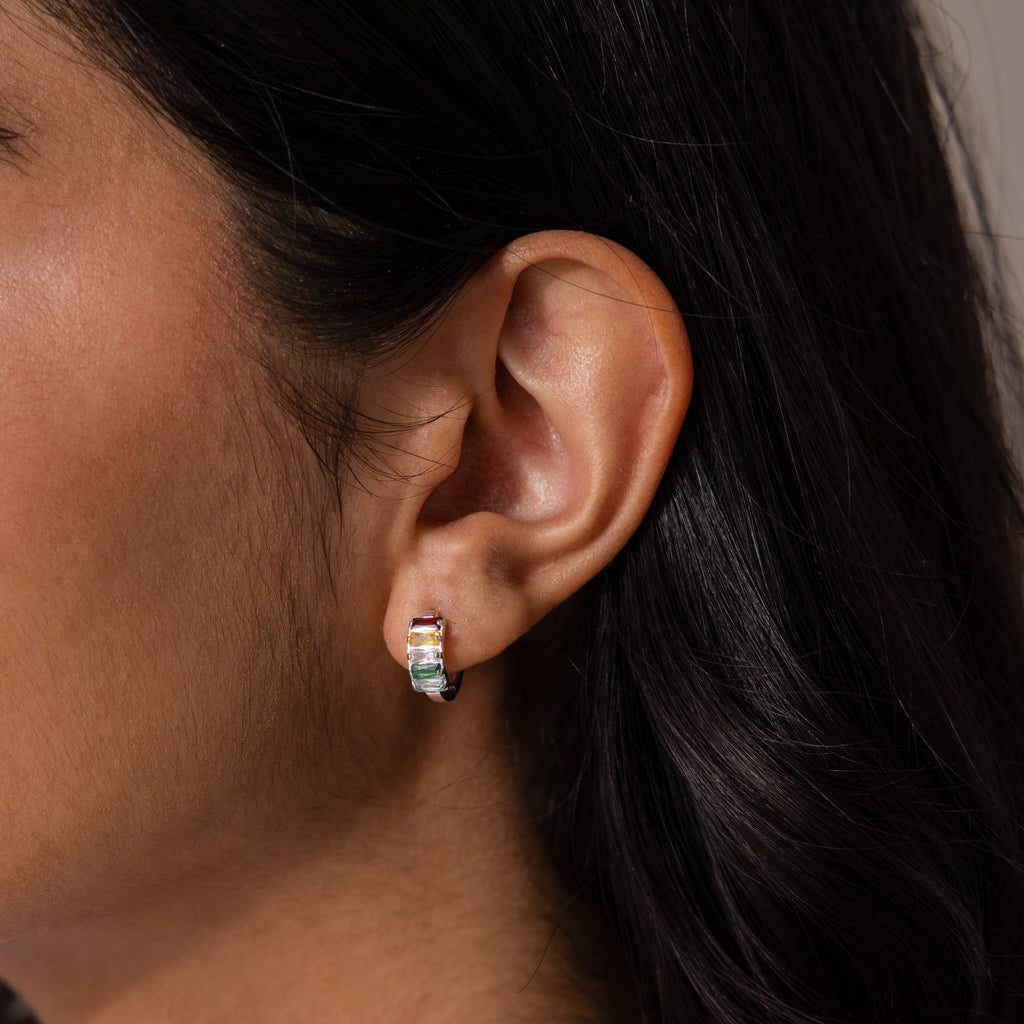 Close-up of a woman’s ear wearing Multiple Baguette Birthstone Huggies in Sterling Silver—petite hoops featuring colorful gemstones, ideal for those who love vibrant jewelry.
