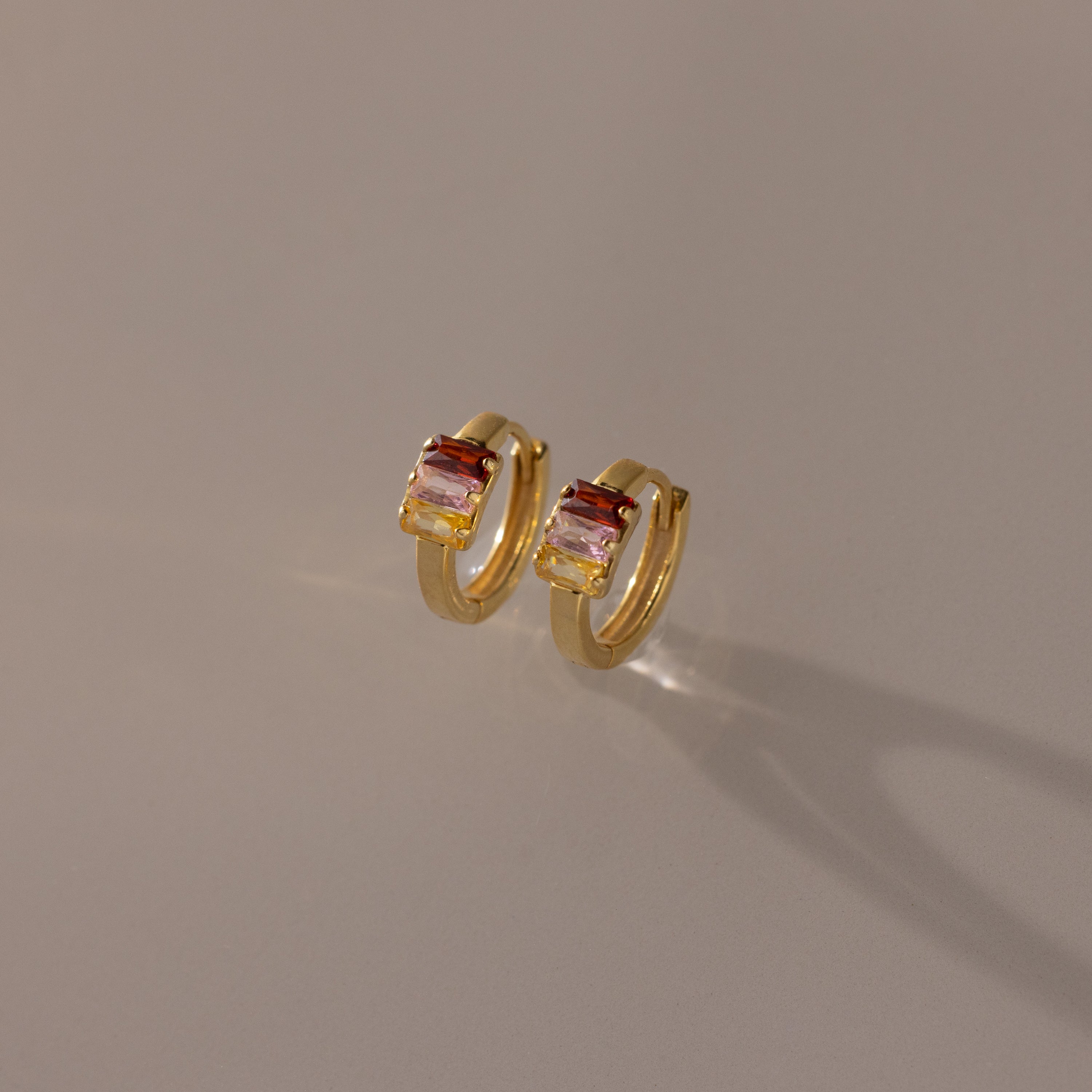 Multiple Baguette Birthstone Huggies in 18K Gold shown on a neutral background, perfect for adding a pop of colorful elegance to any outfit.