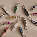 A variety of colorful birthstone charms, including the Ombre Lace Alexandrite Charm, arranged in a circle on a neutral surface.