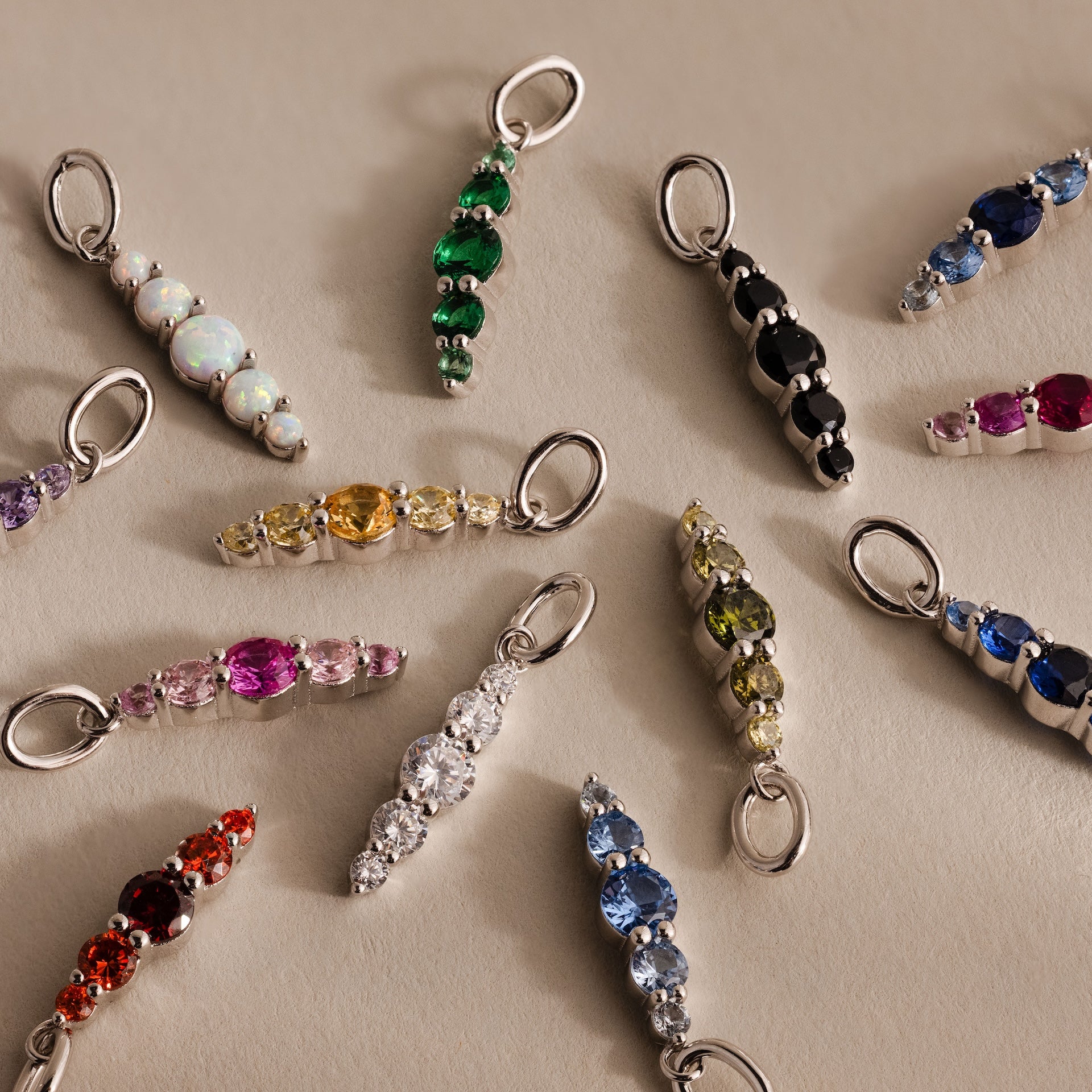 A variety of colorful birthstone charms, including the Ombre Lace Alexandrite Charm, arranged in a circle on a neutral surface.